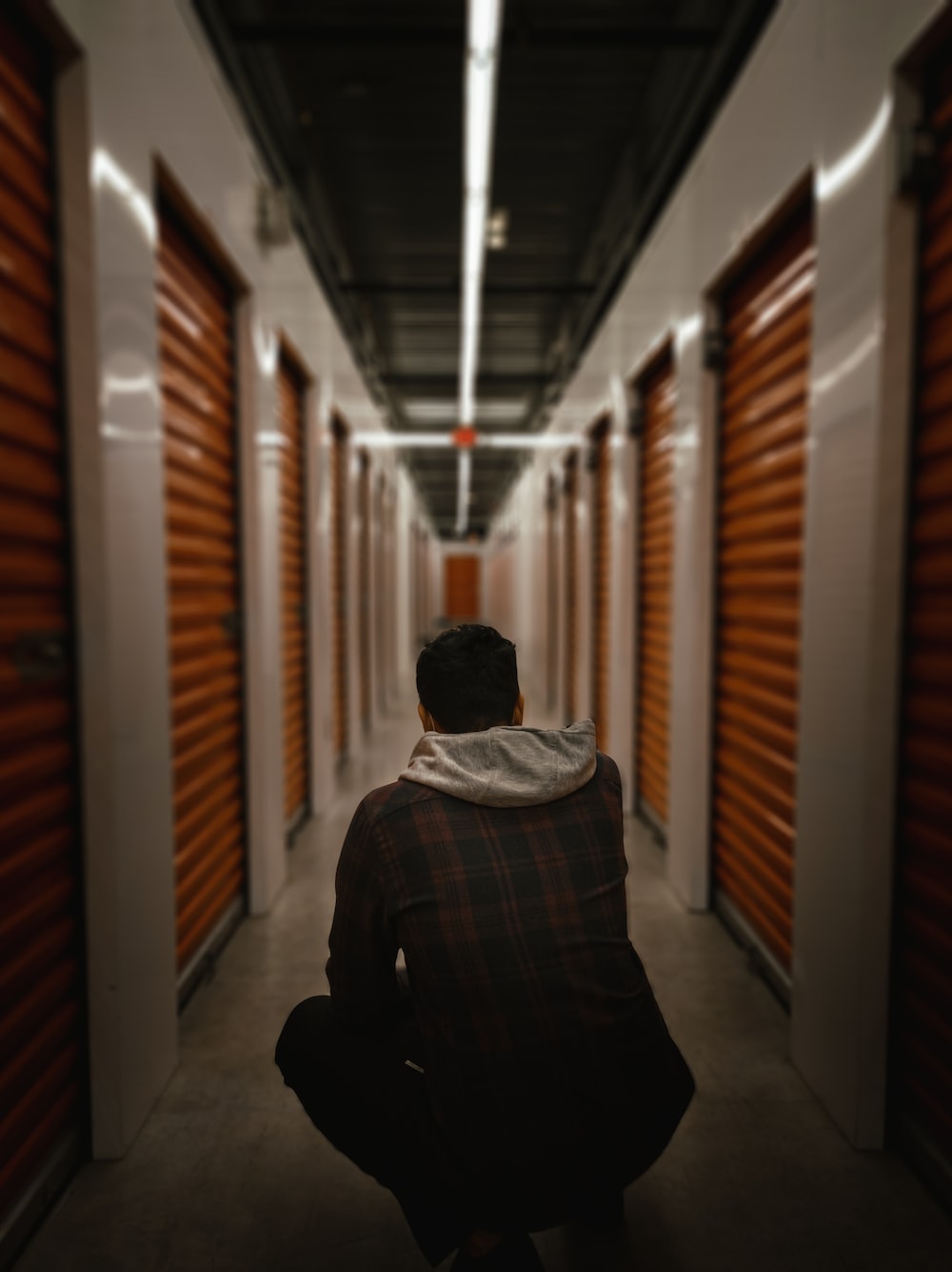 a man sitting in a hallway between two rows of storage units
